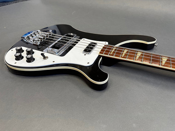 Black electric guitar with white pickguard and chrome hardware, showing control knobs and wooden fretboard on gray background