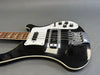 Close-up of black electric bass guitar with white pickguard, chrome bridge, and control knobs on gray background