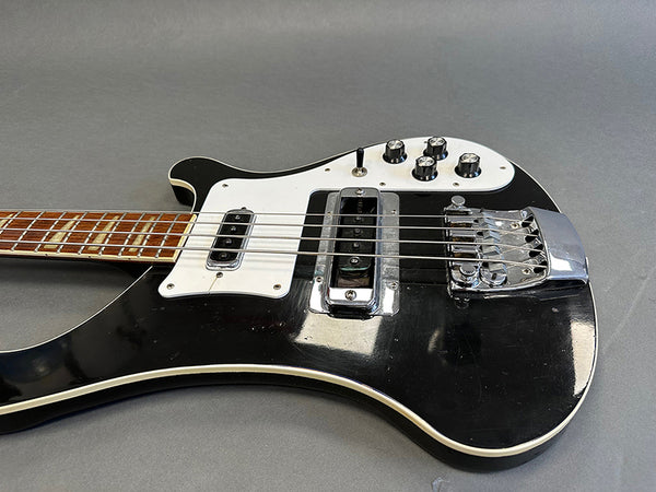 Close-up of black electric bass guitar with white pickguard, chrome bridge, and control knobs on gray background