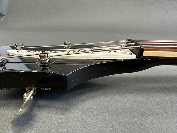 Close-up of black guitar headstock with vintage metal tuning pegs and white truss rod cover on grey background