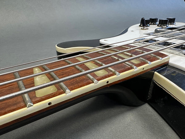 Close-up of electric bass guitar fretboard with metal frets, large triangular inlays, and steel strings against a black and white body background.