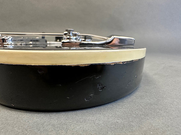 Close-up of a black electric guitar body edge showing chips and wear on the paint and cream binding with a chrome tremolo bar on a gray background.