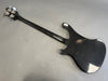 Black electric bass guitar showing worn and scratched back with four tuning pegs on headstock on gray background