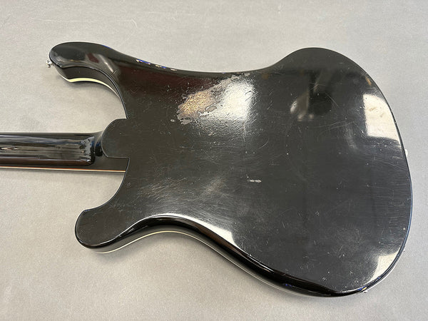 Black electric guitar body with worn finish and visible scratches, shown from the back.