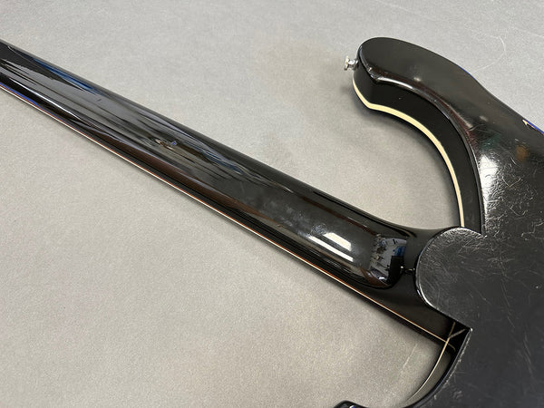 Close-up of black electric guitar neck joint and body with cream binding and visible wear scratches on gray background