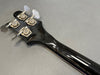 Back of black bass guitar headstock with four tuning pegs on gray background