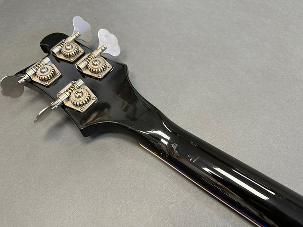 Back of black bass guitar headstock with four tuning pegs on gray background