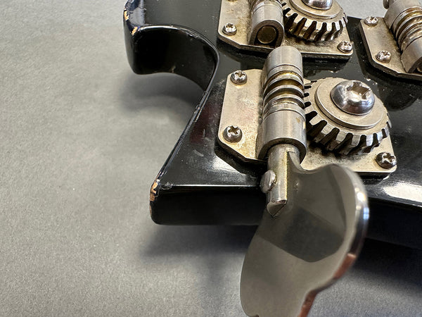 Close-up of vintage black electric guitar tuning pegs with visible wear and metal gears on gray background