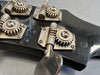 Close-up of vintage guitar tuners on black headstock with metal tuning gears and screws