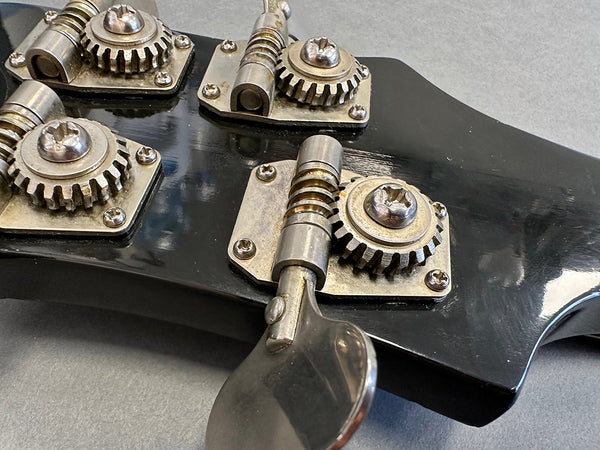 Close-up of vintage guitar tuners on black headstock with metal tuning gears and screws