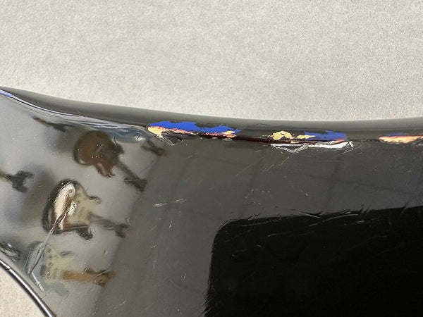 Close-up of chipped and worn black guitar body finish showing paint damage and cracks on top edge