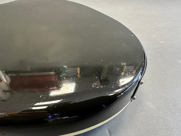 Close-up of black guitar body corner with visible scratches and paint chips on a gray surface