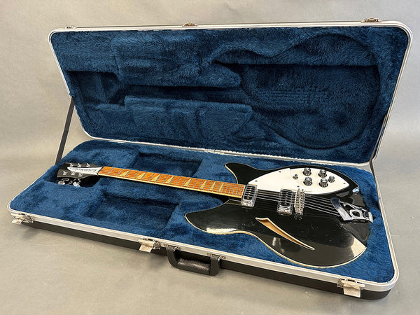 Black semi-hollow body electric guitar with white pickguard and maple fretboard in blue plush-lined hard case on gray background