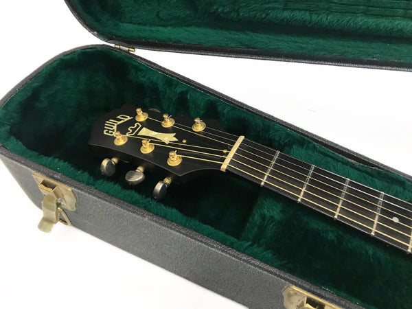 Guild acoustic guitar headstock with gold tuning pegs inside green plush lined black guitar case