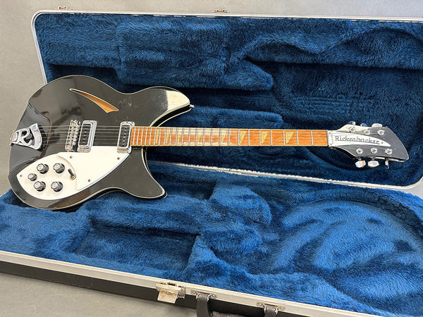 Vintage black Rickenbacker electric guitar with white pickguard and trapezoid inlays resting in blue plush lined hard case