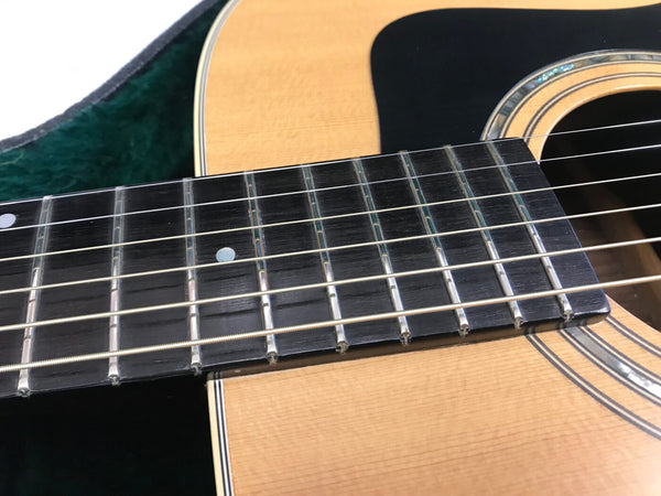 Close-up view of acoustic guitar fretboard and soundhole with steel strings and dot inlays, natural wood finish and black pickguard
