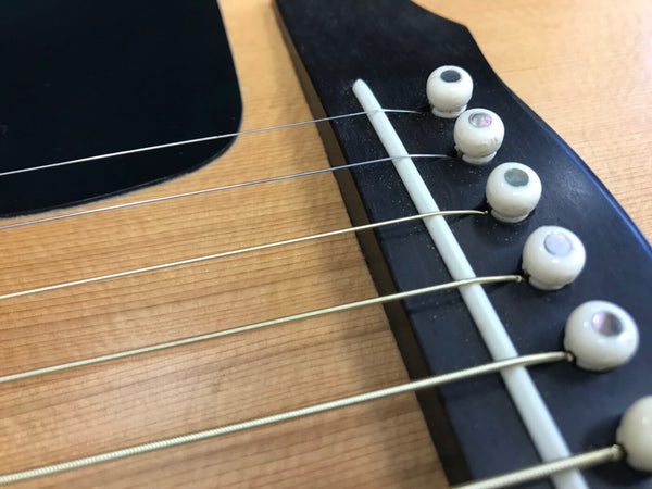 Close-up of acoustic guitar bridge with white bridge pins and metal strings on natural wood finish top