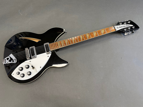 Black Rickenbacker electric guitar with white pickguard and chrome hardware on gray background