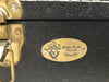 Close-up of black guitar case latch with brass Guild logo plate and "Made To Be Played" engraving on the front