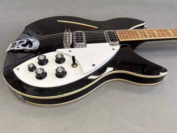Black electric guitar with white pickguard, five black control knobs, metal bridge, and cream binding on body edges, placed on gray surface