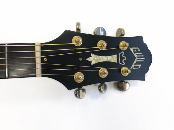 Guild acoustic guitar headstock with gold tuning pegs and mother-of-pearl inlay on black background