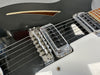 Close-up of black electric guitar bridge and pickups with white pickguard and wooden sound hole detail