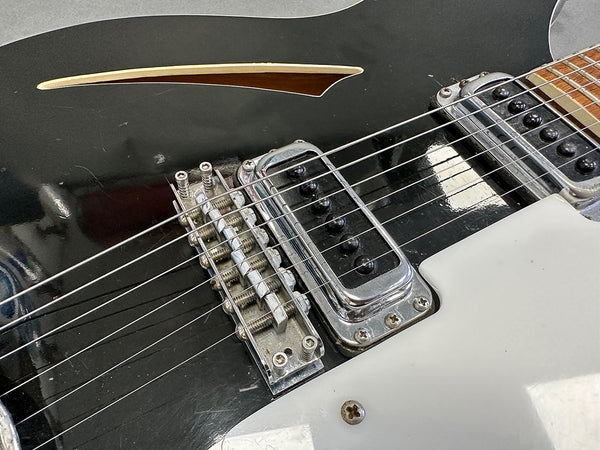 Close-up of black electric guitar bridge and pickups with white pickguard and wooden sound hole detail