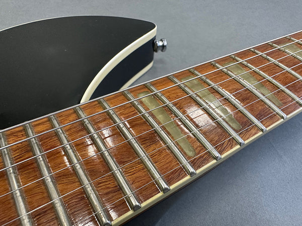 Close-up of electric guitar rosewood fretboard with white binding and metal frets on black guitar body background