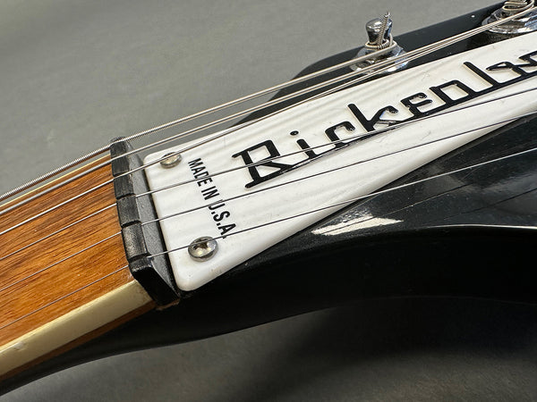 Close-up of Rickenbacker electric guitar headstock with "Made in U.S.A." label and steel strings, showing wood neck and black body finish.