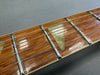 Close-up of guitar fretboard with metal frets, six strings, and triangular mother-of-pearl inlay on polished wood fingerboard