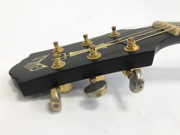 Close-up of black guitar headstock with gold tuning pegs and strings on white background