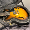 Sunburst semi-hollow electric guitar with dual humbucker pickups in a plush gray-lined hard case