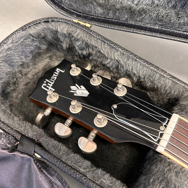 Close-up of black Gibson guitar headstock with tuning pegs and logo inside plush-lined guitar case