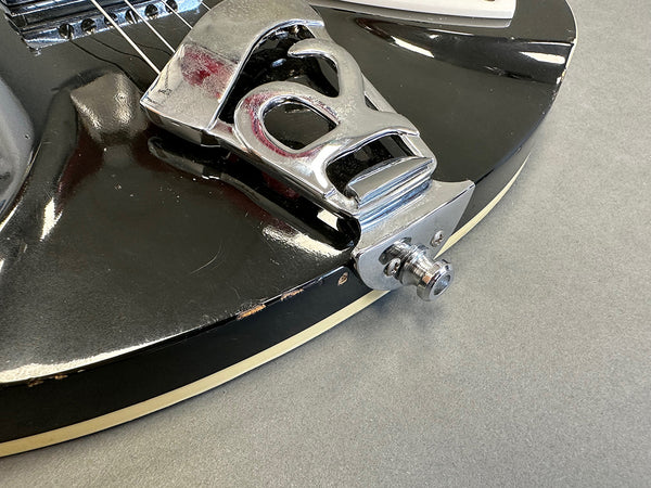 Close-up of black electric guitar body with chrome tailpiece and visible wear on edges, showcasing vintage-style guitar hardware.