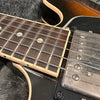 Close-up image of electric guitar fretboard and pickup showing metal strings, dot inlays, and vintage humbucker pickup with worn metal cover on black guitar body