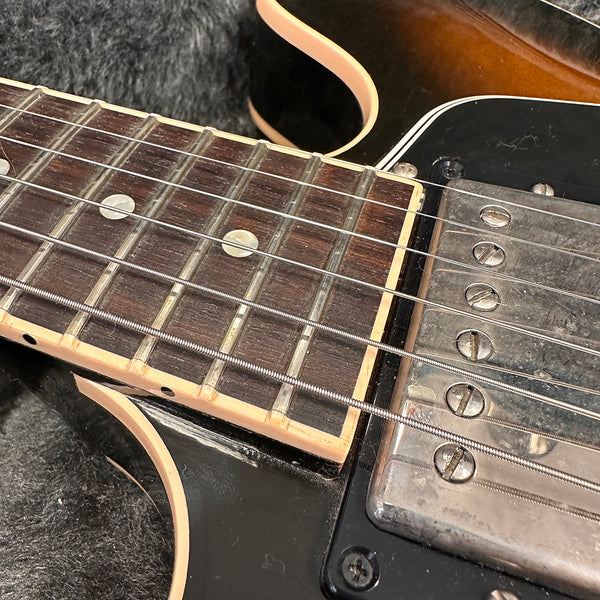 Close-up image of electric guitar fretboard and pickup showing metal strings, dot inlays, and vintage humbucker pickup with worn metal cover on black guitar body