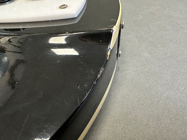 Close-up of black electric guitar body corner showing worn edges and scratches on finish