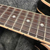Close-up of rosewood guitar fretboard with metal frets, mother-of-pearl dot inlays, and steel strings on black electric guitar body