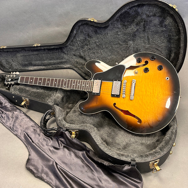 Vintage sunburst semi-hollow electric guitar with dual humbucker pickups inside a black plush-lined hard shell guitar case with satin cloth cover.