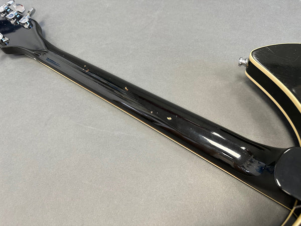 Black guitar neck with cream binding and visible minor wear and scratches, close-up view of back side on gray background