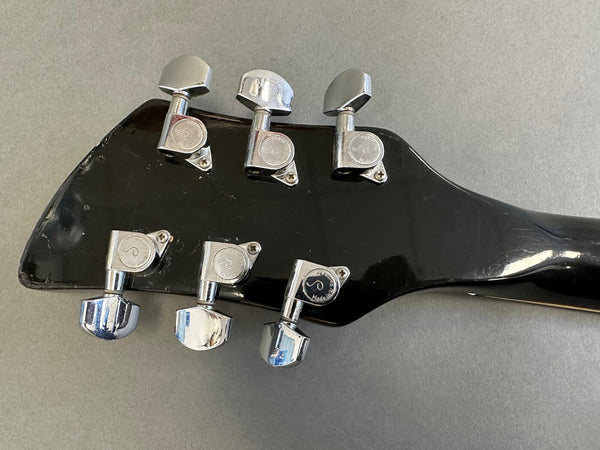 Close-up of black guitar headstock with six chrome tuning pegs showing wear and scratches on gray background