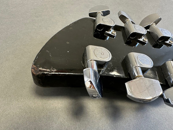 Close-up of black guitar headstock with chrome tuning pegs showing wear and damage on edge, suitable for Coffee House Guitars product listing.