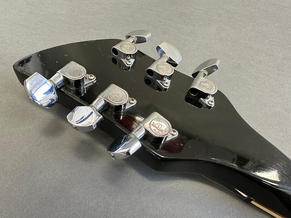 Close-up of black guitar headstock with six chrome tuning pegs on gray background, showing tuning machines and brand logo details