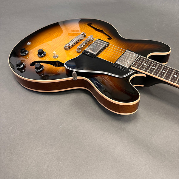 Hollow body electric guitar with sunburst finish, black pickguard, dual humbucker pickups, four black control knobs, and rosewood fretboard on gray background