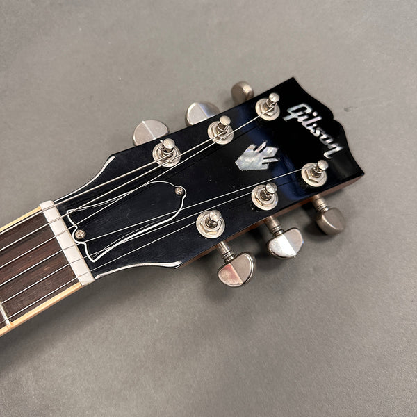 Close-up of black Gibson guitar headstock with tuning pegs and strings on grey background