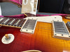 Close-up of Gibson Les Paul electric guitar body showing sunburst finish, humbucker pickups, toggle switch labeled Rhythm and Treble, and part of the guitar neck with inlays.