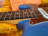 Close-up of blue electric guitar neck with rosewood fretboard, metal frets, and white dot inlays over an orange plush guitar case lining and tortoiseshell pickguard near single-coil pickup screws.