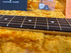 Close-up of electric guitar fretboard and strings with dot inlays, resting on plush yellow guitar case lining, showing maple neck and custom care guitar accessories in the background.