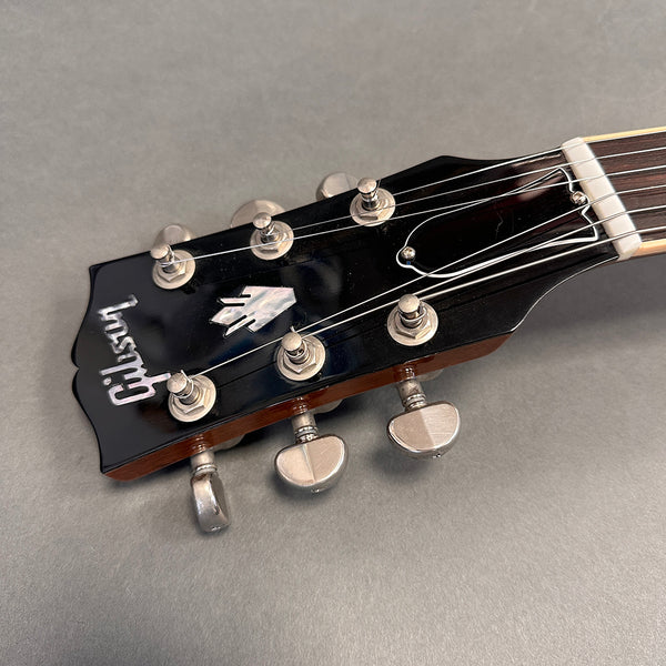 Close-up of Gibson guitar black headstock with tuning pegs and strings against gray background