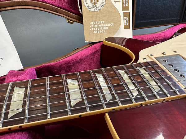 Close-up of Gibson electric guitar neck with mother-of-pearl block inlays and metal frets, resting in pink velvet-lined hard case with Gibson dealer quality and performance tags.
